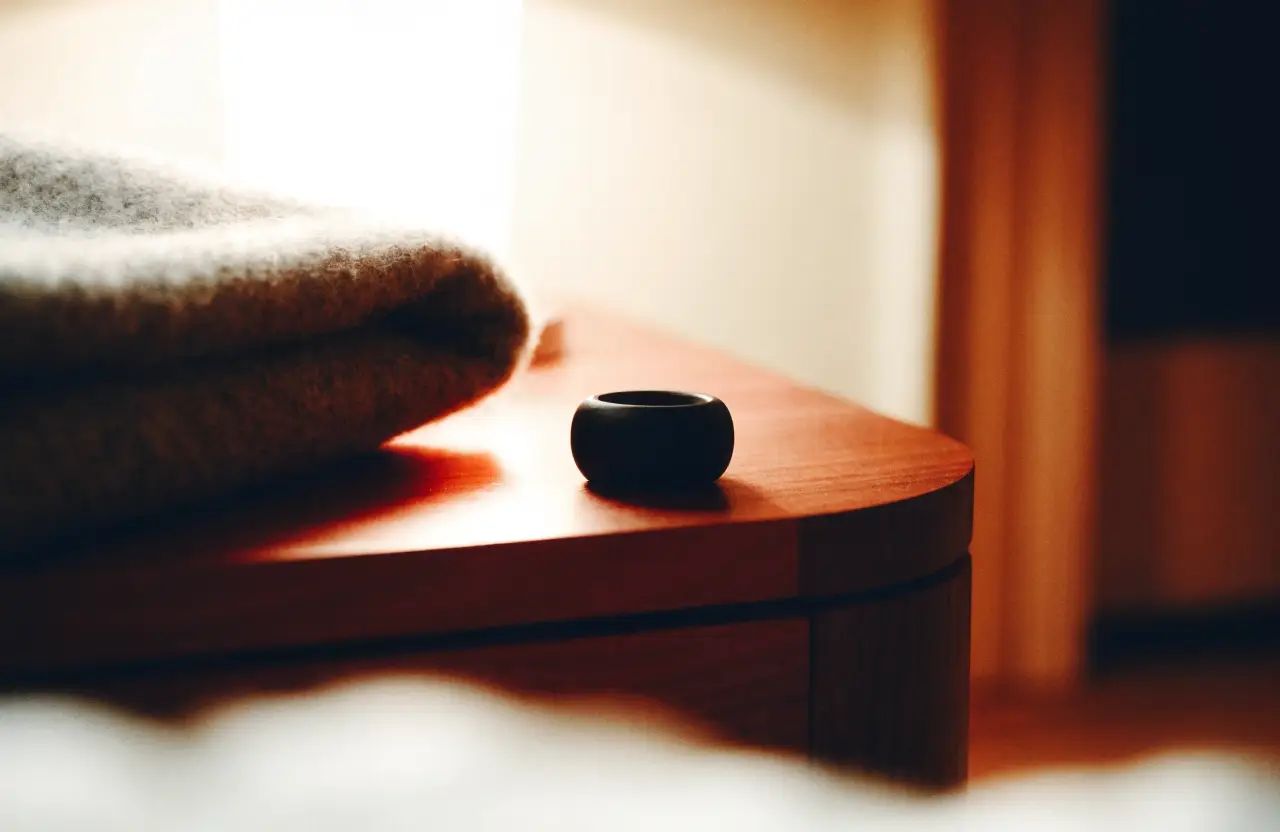 A smart ring on a dark nightstand beside a folded blanket
