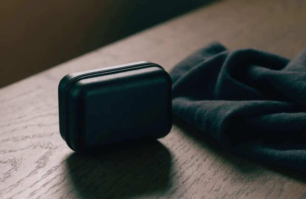 A small matte black zip case, closed, on a dark oak surface