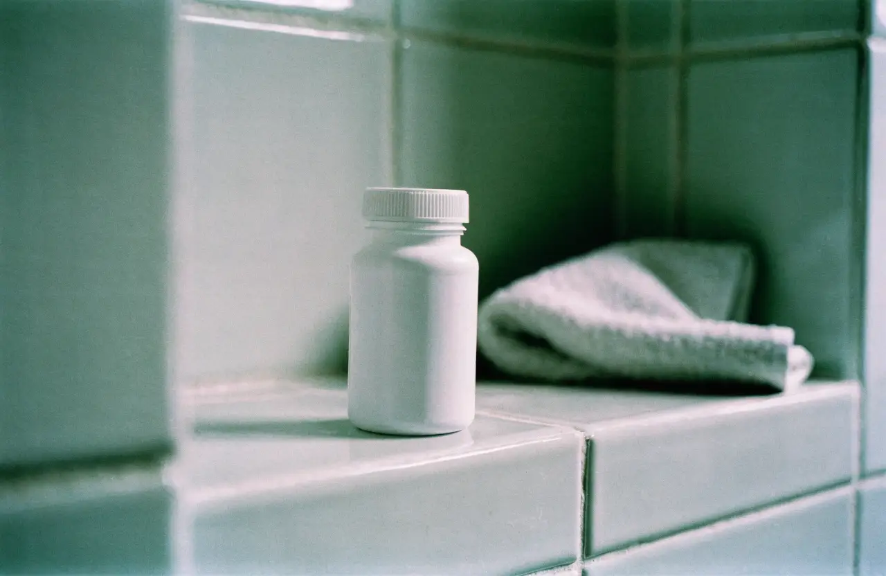 A plain white pill bottle on a pale tiled bathroom shelf