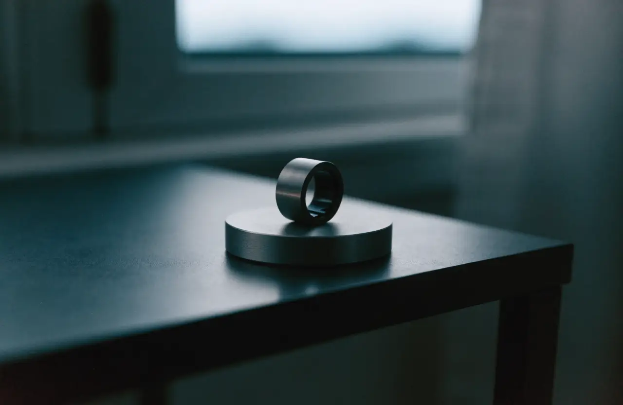 A titanium smart ring on its charging puck on a dark nightstand